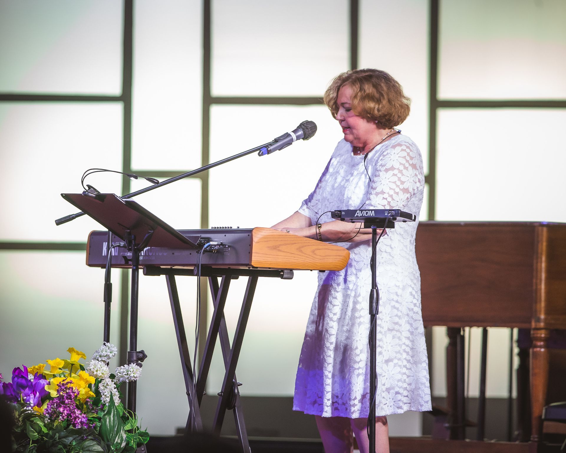 A woman in a white dress is playing a keyboard and singing into a microphone.