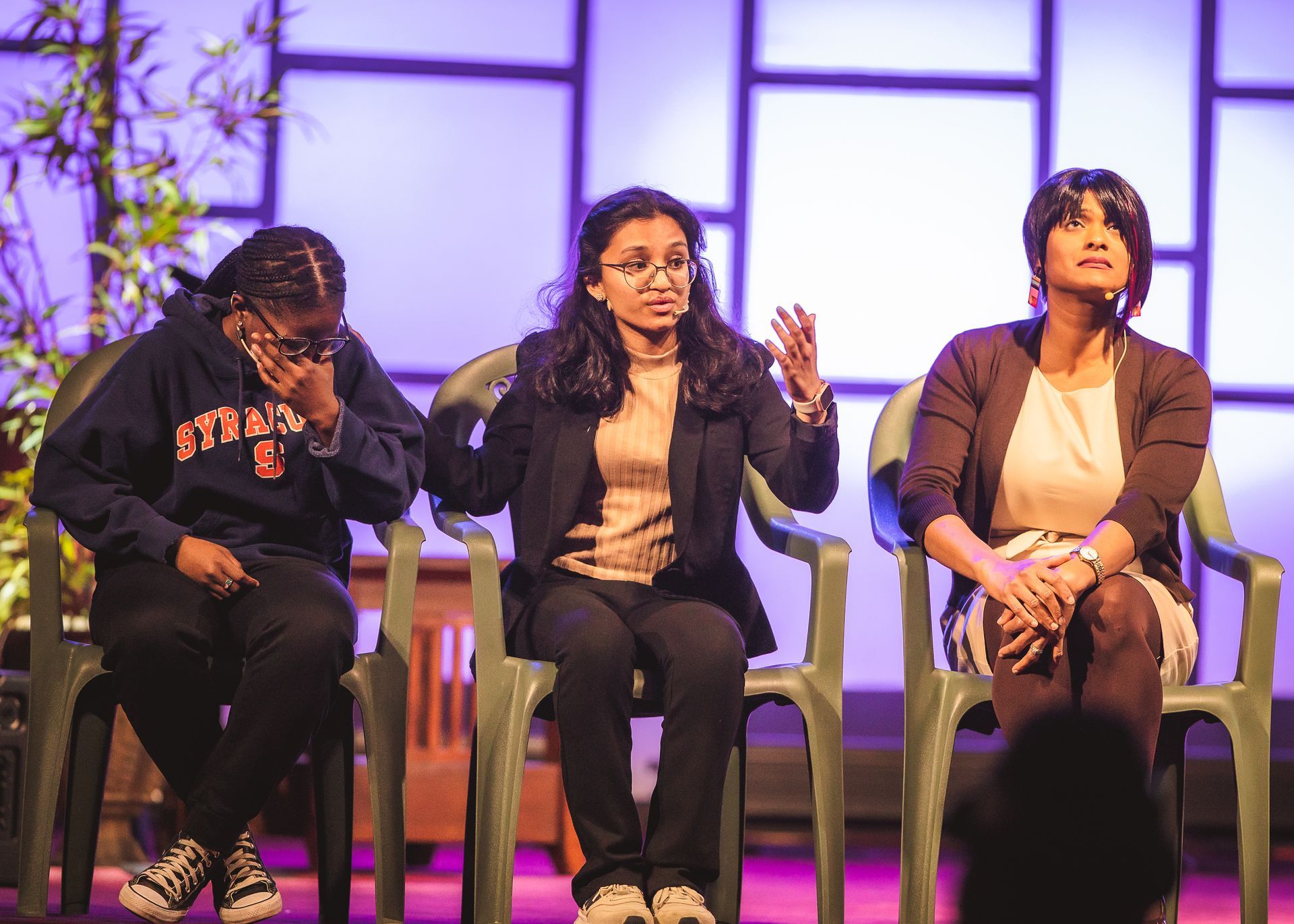 Three women are sitting in chairs on a stage.