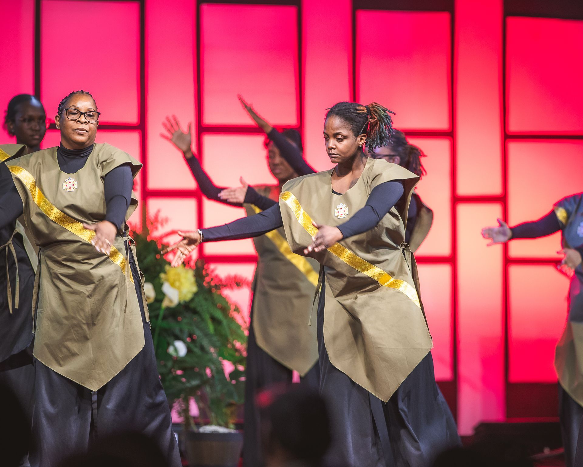 A group of women are dancing on a stage in front of a red background.