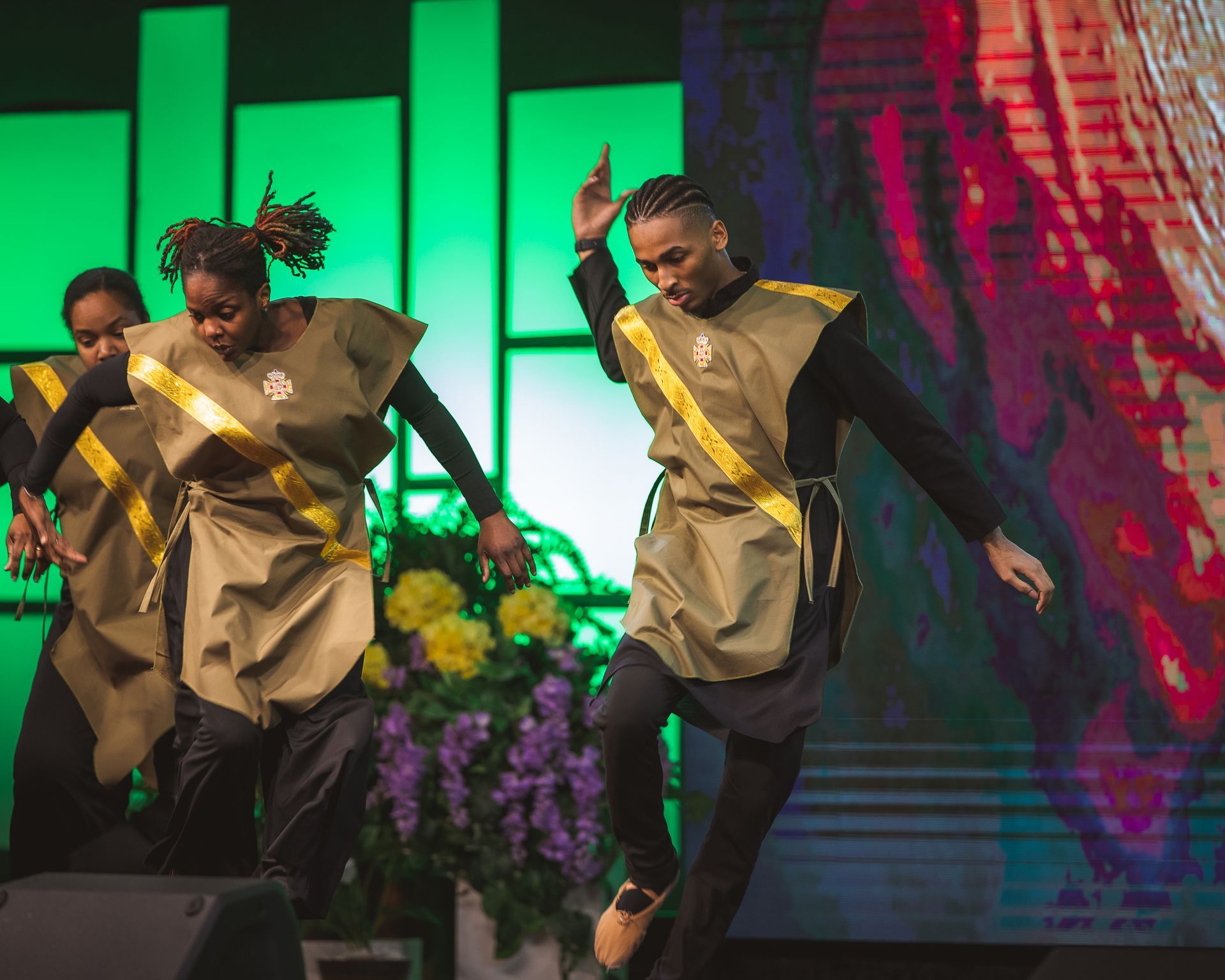A group of people are dancing on a stage in front of a large screen.