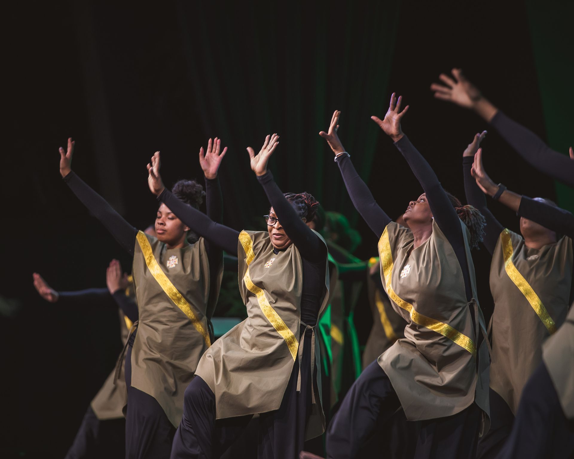 A group of women are dancing on a stage with their arms in the air.