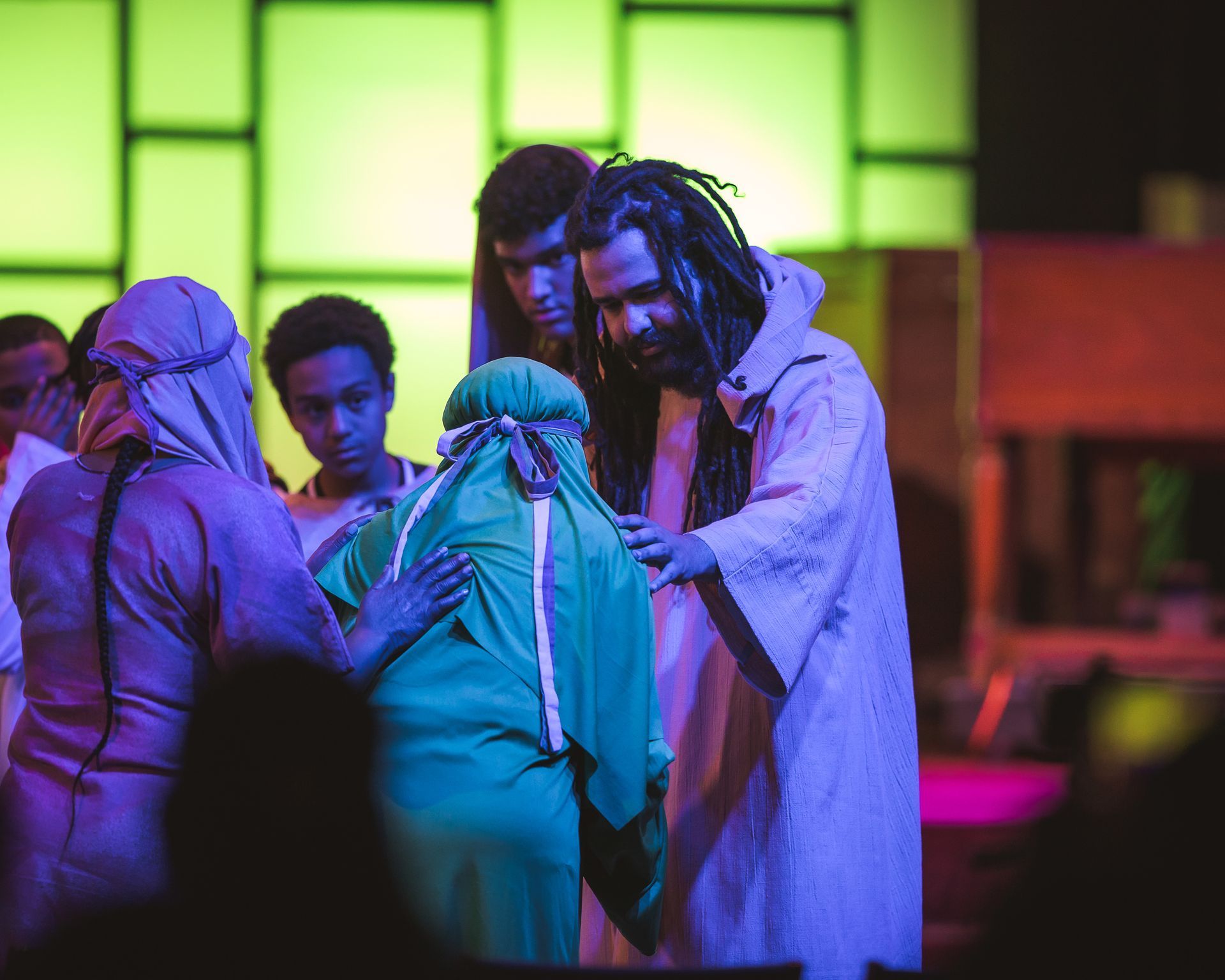 A group of people are standing around jesus on a stage.