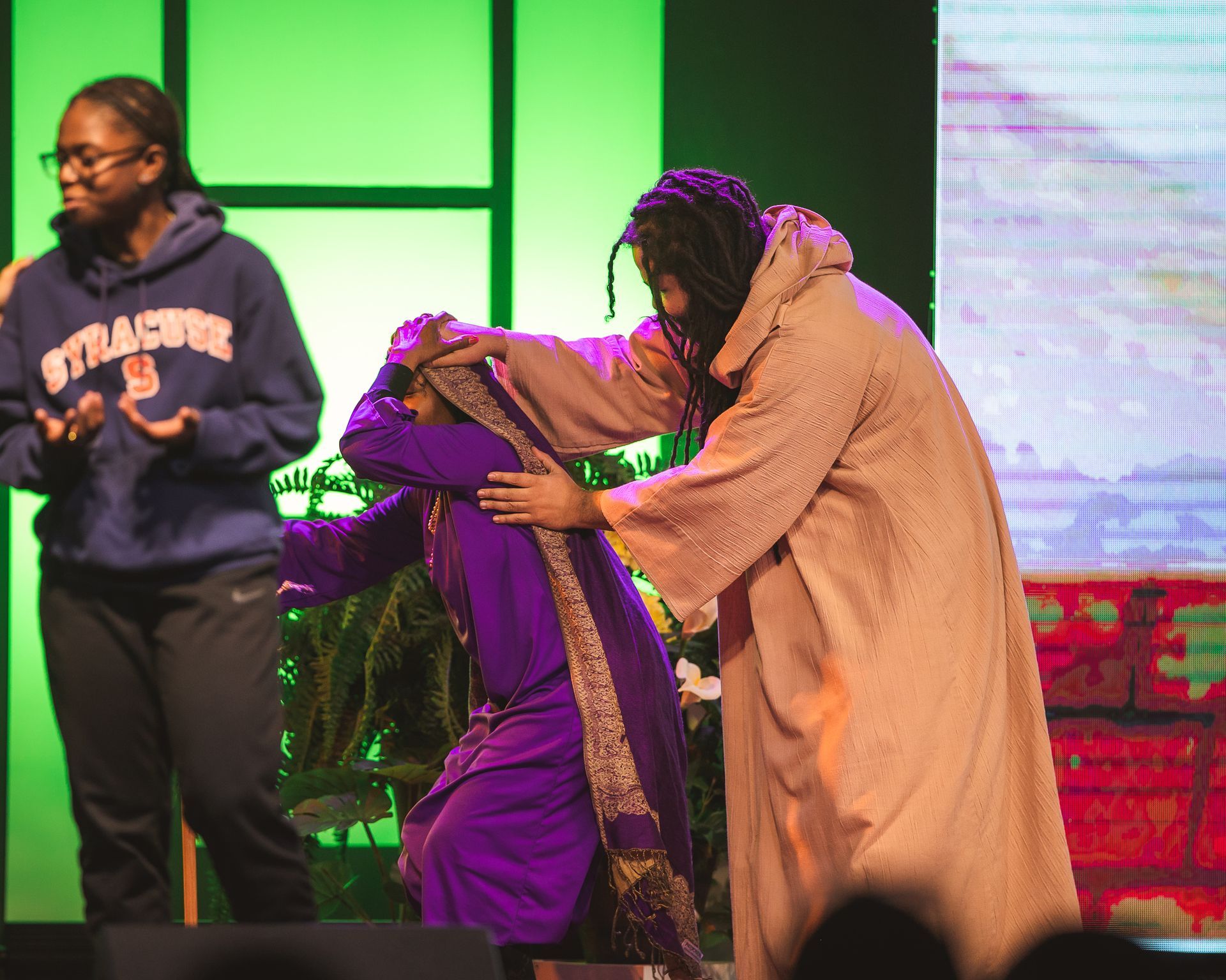 A woman in a strasburg sweatshirt is standing next to a man in a robe on a stage.