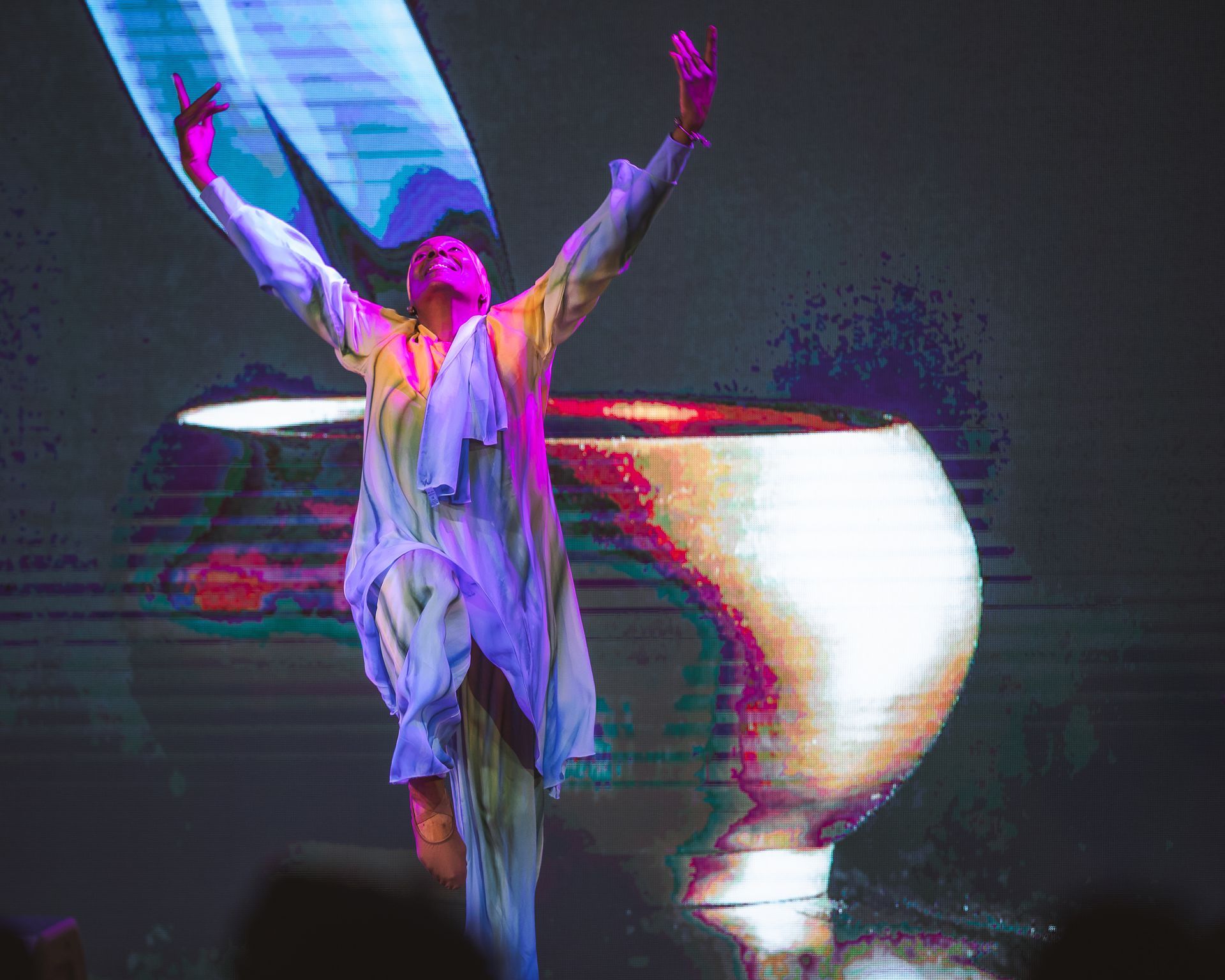 A man is dancing in front of a large screen with his arms outstretched.