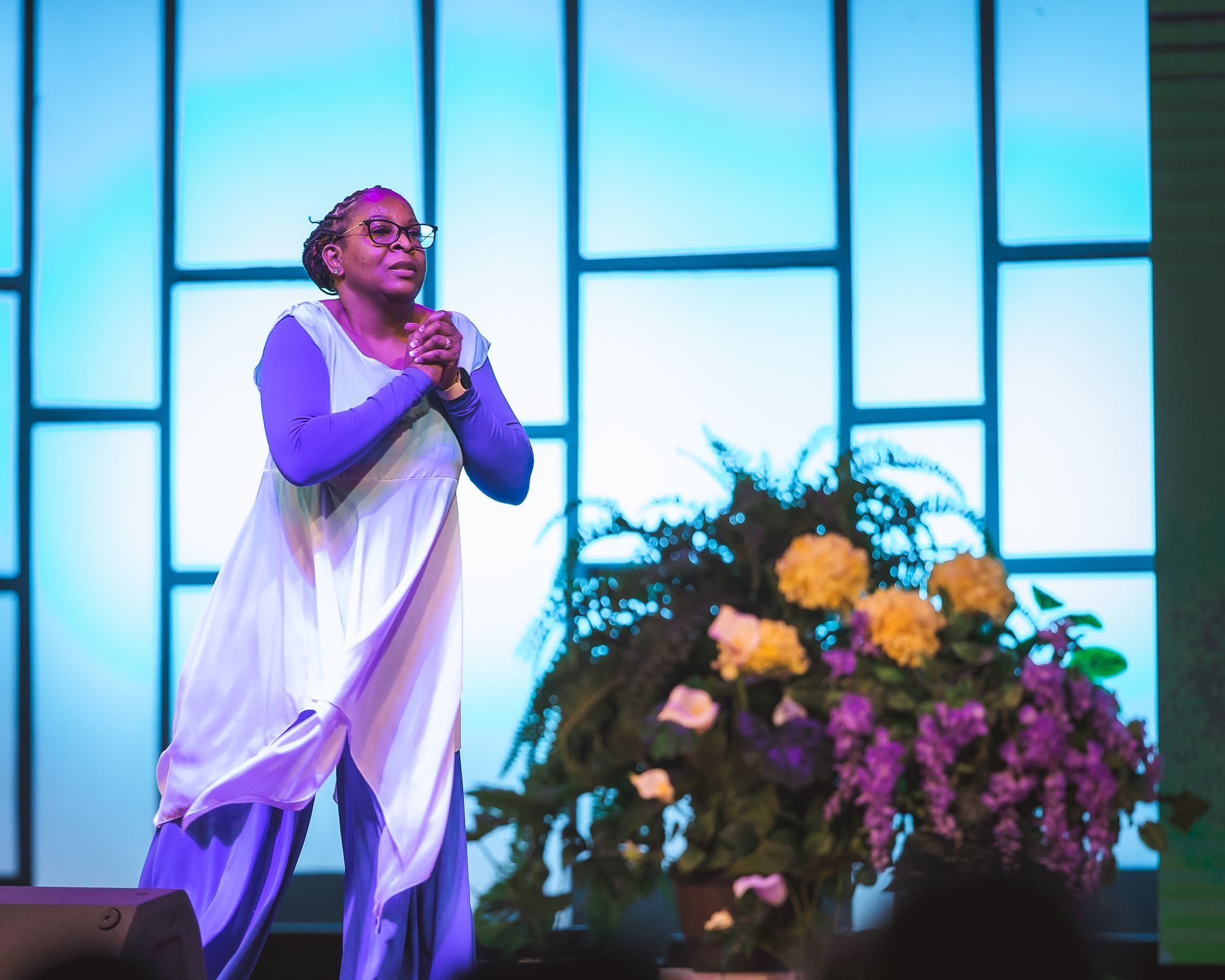 A woman is standing on a stage holding a microphone and praying.