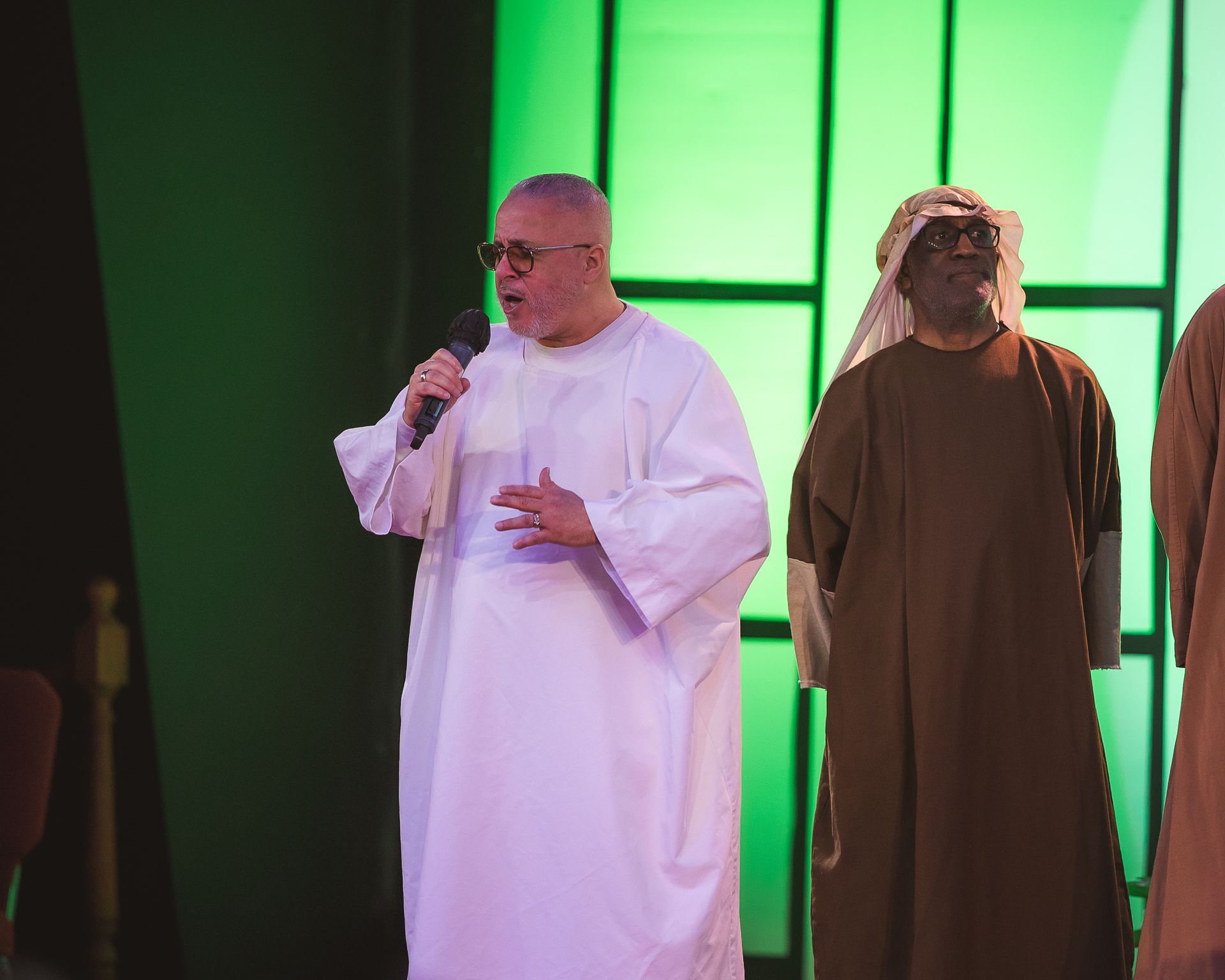 A man in a white robe is singing into a microphone on a stage.