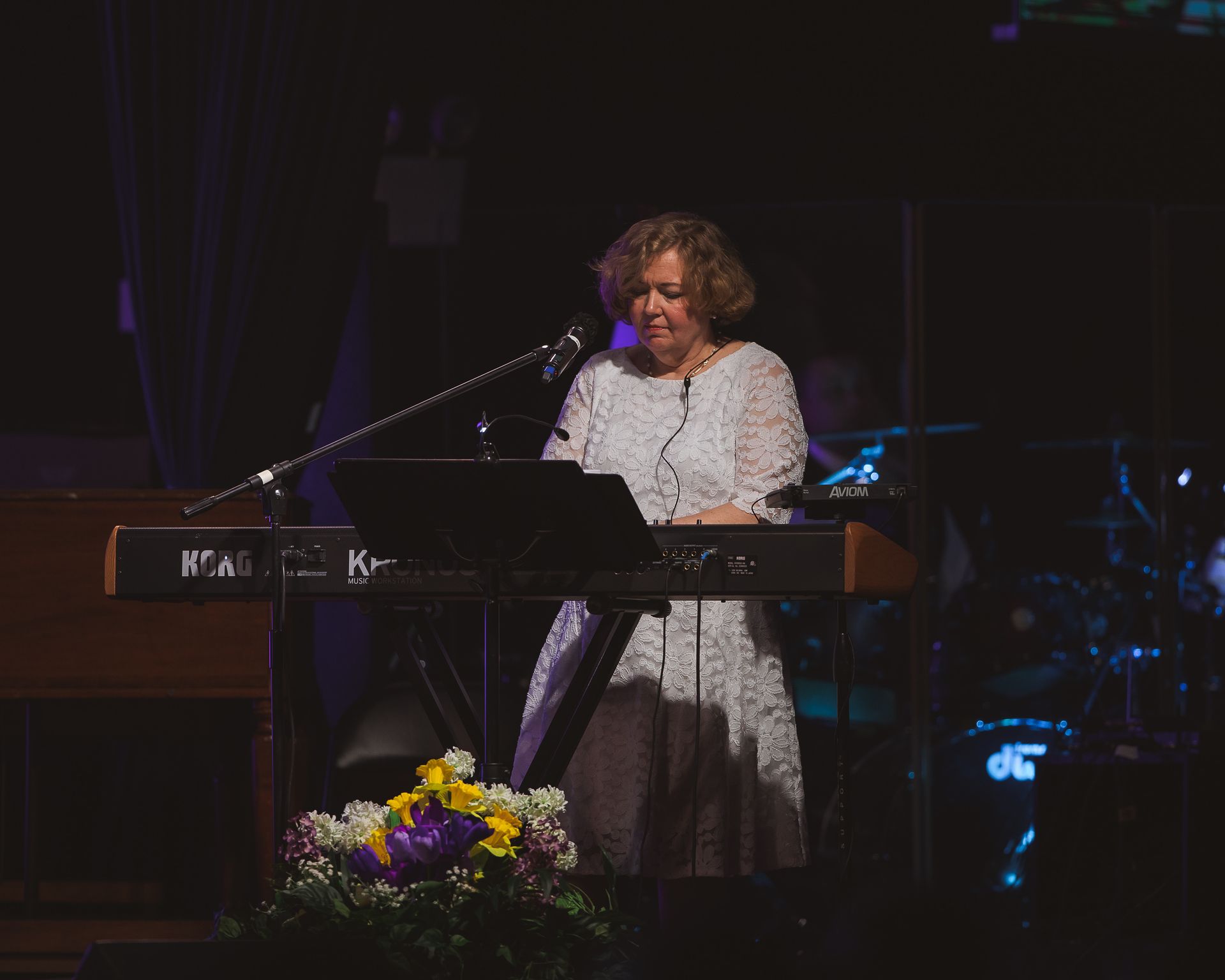 A woman is playing a keyboard and singing into a microphone on a stage.