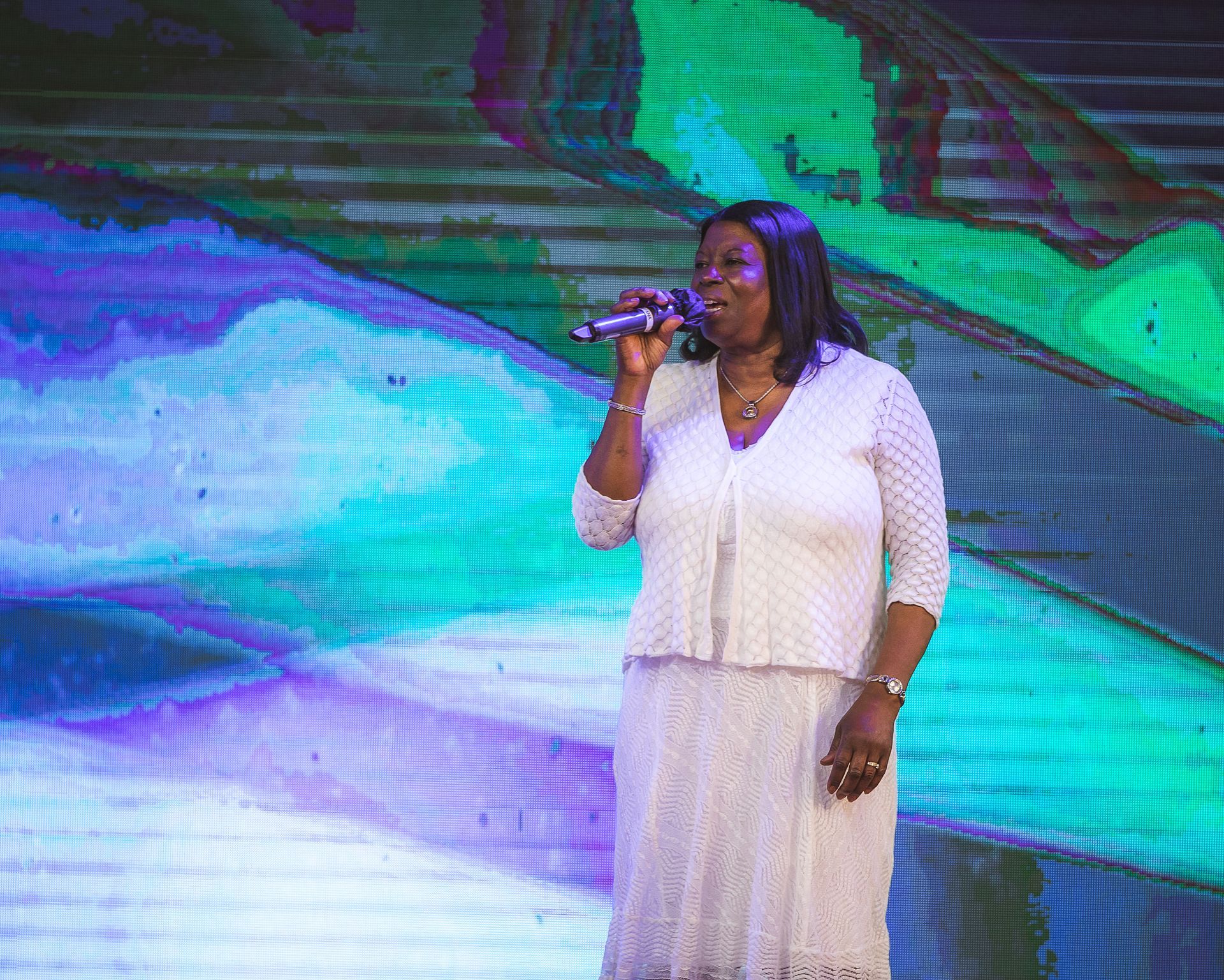 A woman in a white dress is singing into a microphone on a stage.