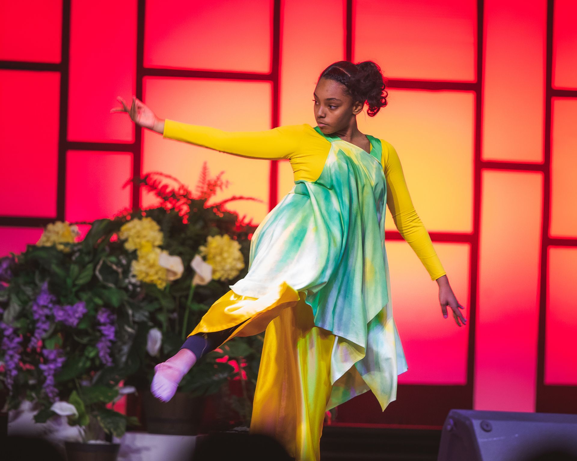 A woman in a yellow and green dress is dancing on a stage.