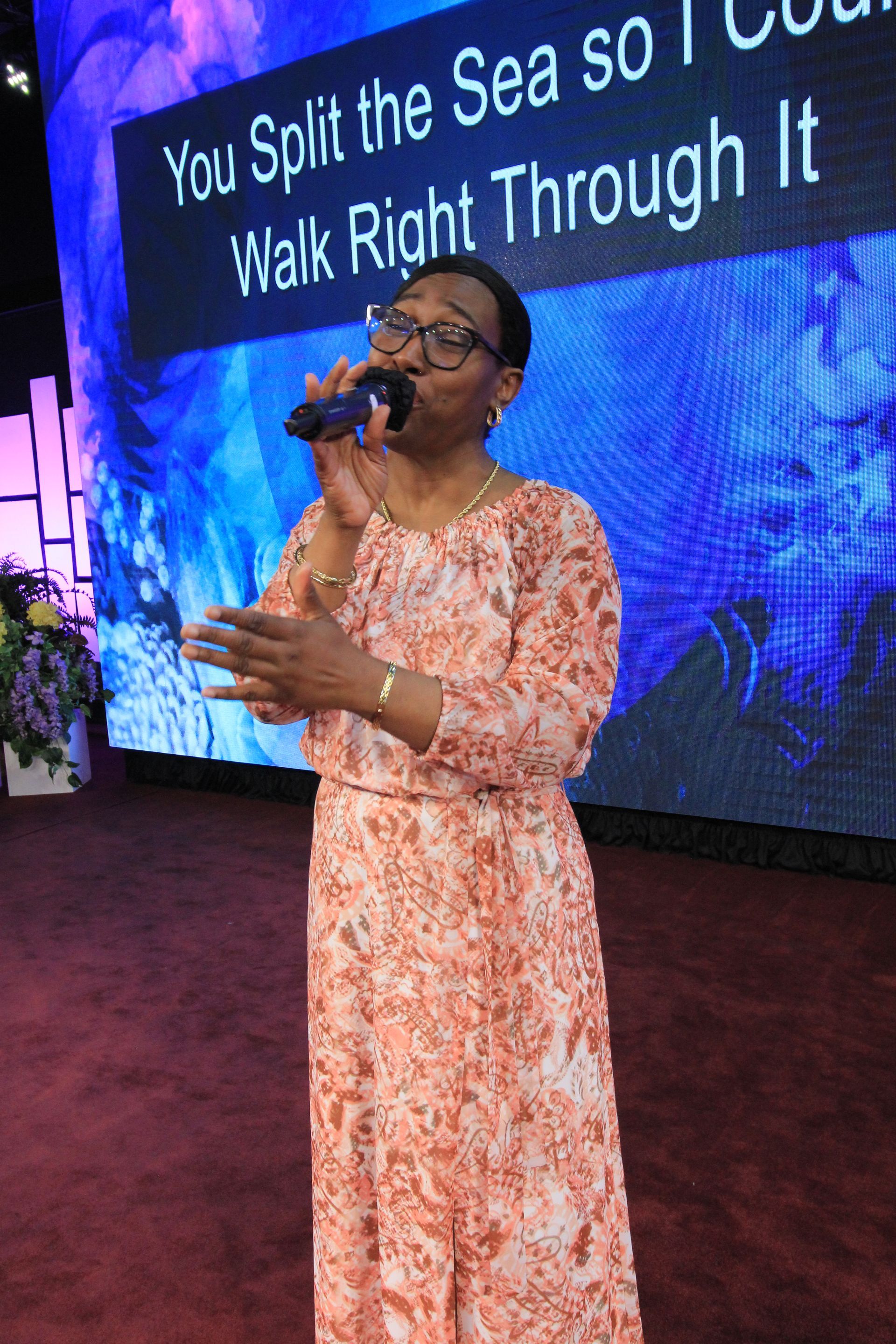 a woman singing into a microphone in front of a sign that says you split the sea so walk right through it