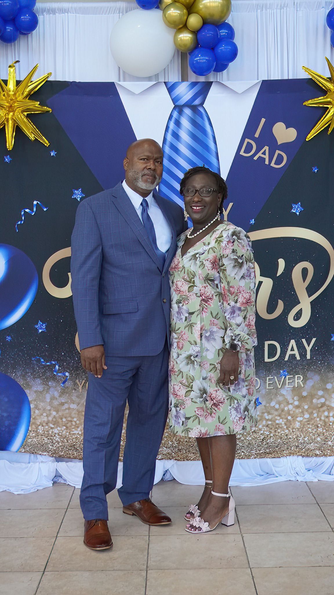 A man and a woman are posing for a picture in front of a father 's day backdrop.