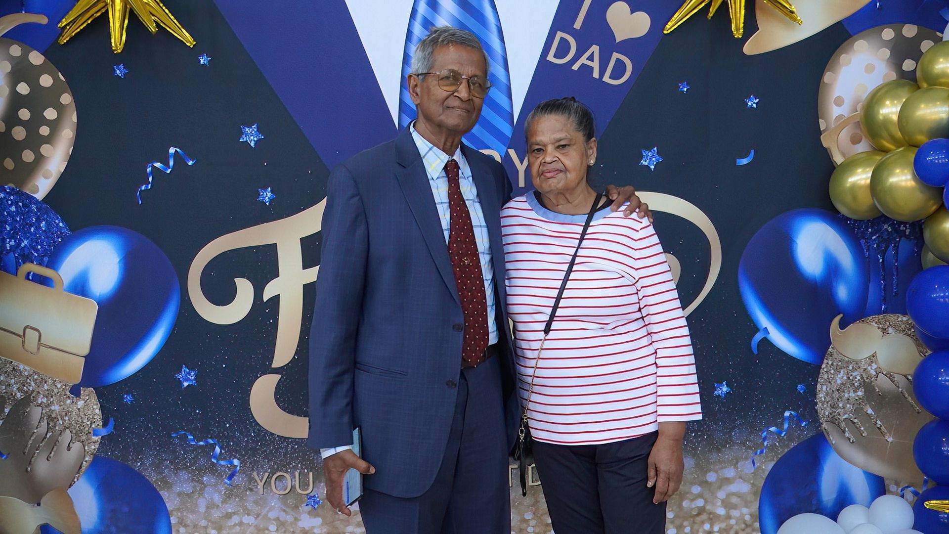 A man and a woman are posing for a picture in front of balloons.
