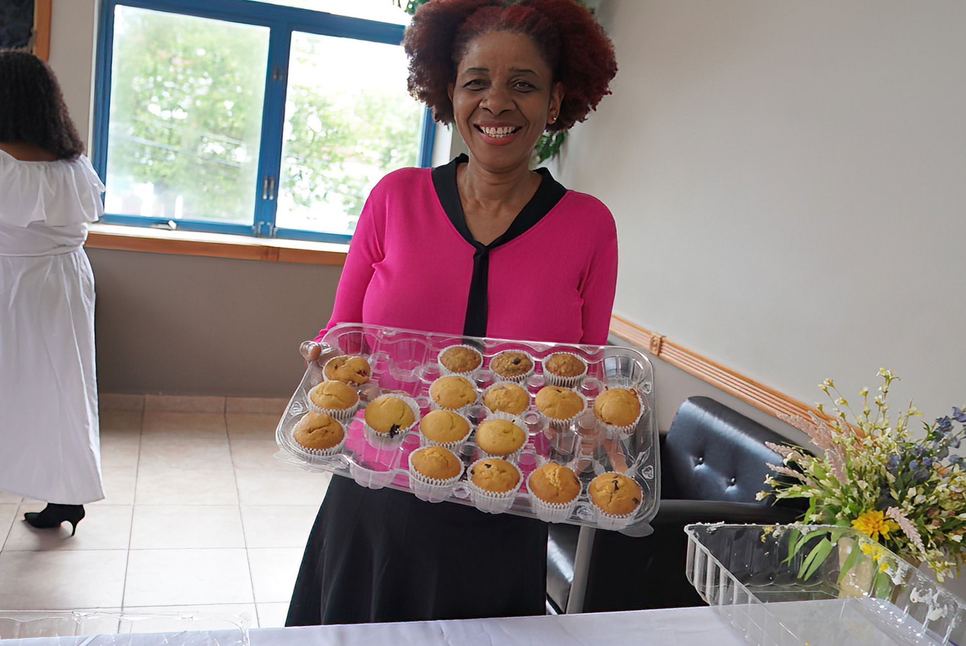 A woman in a pink shirt is holding a tray of cupcakes.