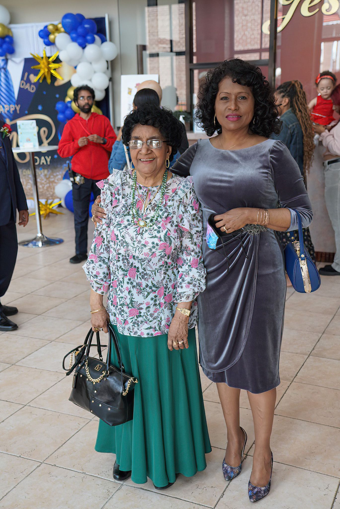 Two women are posing for a picture in a room with balloons in the background.