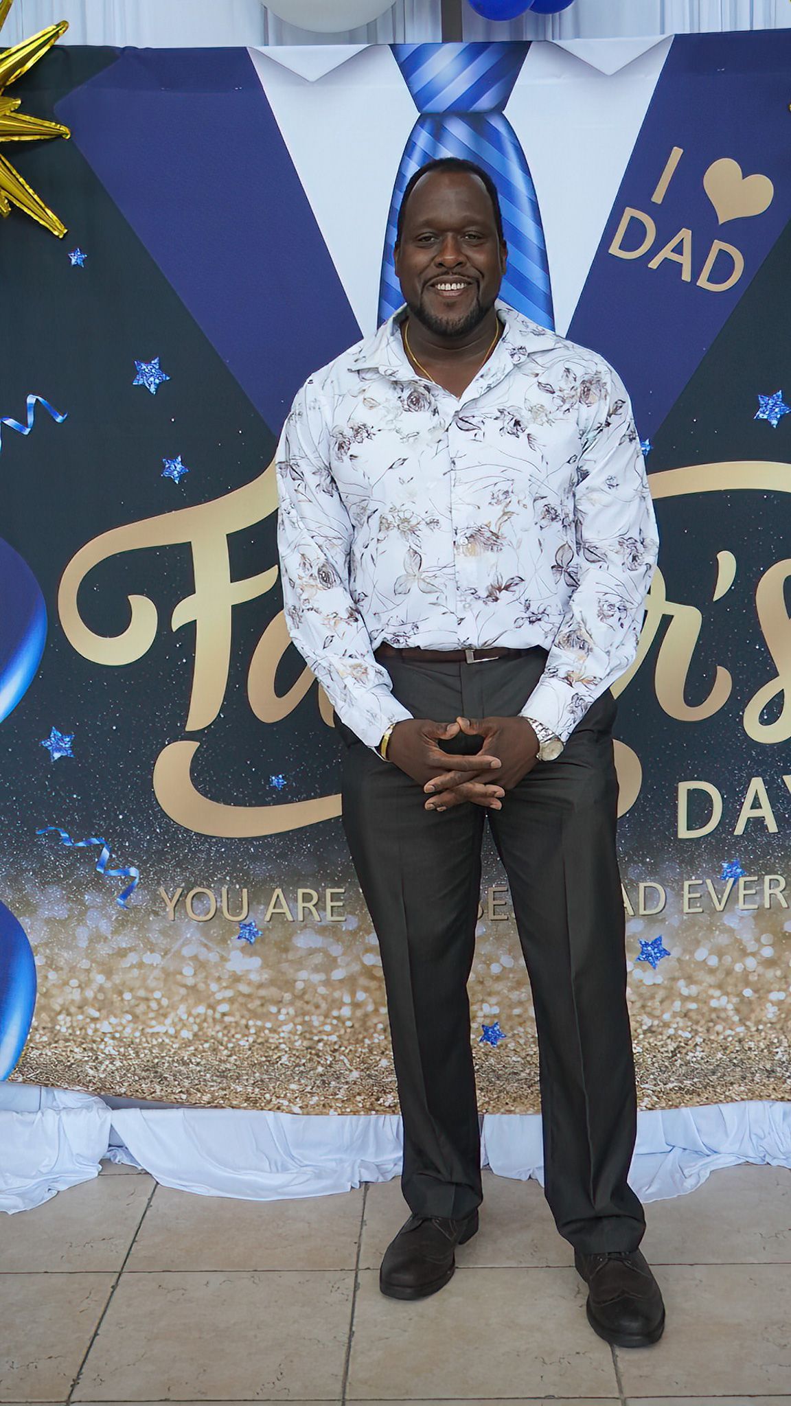 A man in a white shirt and black pants is standing in front of a father 's day sign.