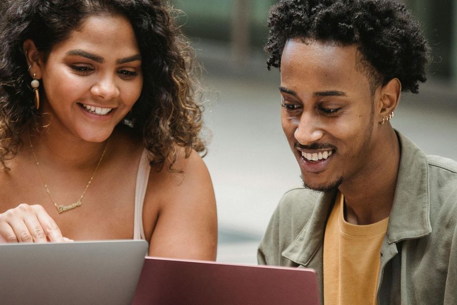 A man and a woman are smiling while looking at a laptop computer.