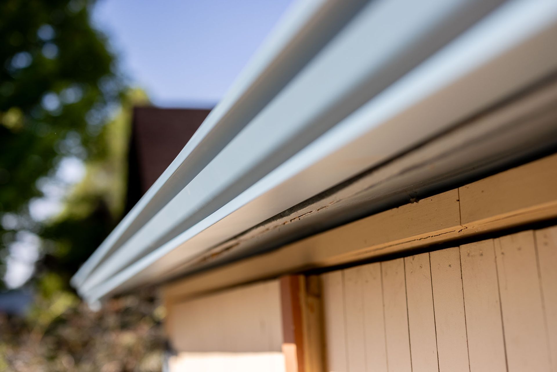 A close-up of a metal gutter attached to the edge of a light-colored wooden building roof, viewed from below.