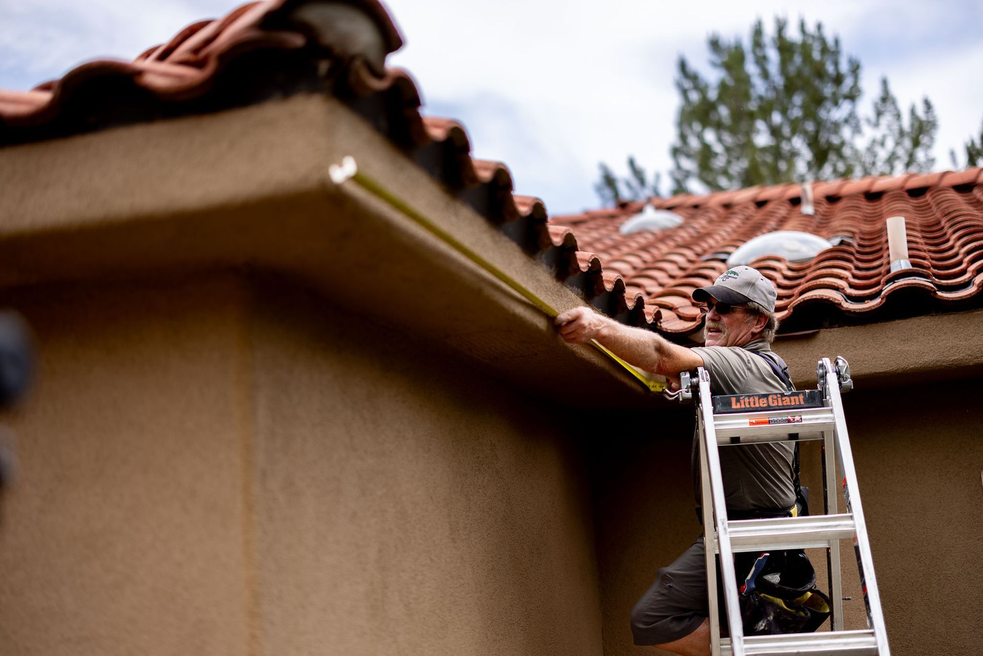 A man is installing a gutter on the side of a house.