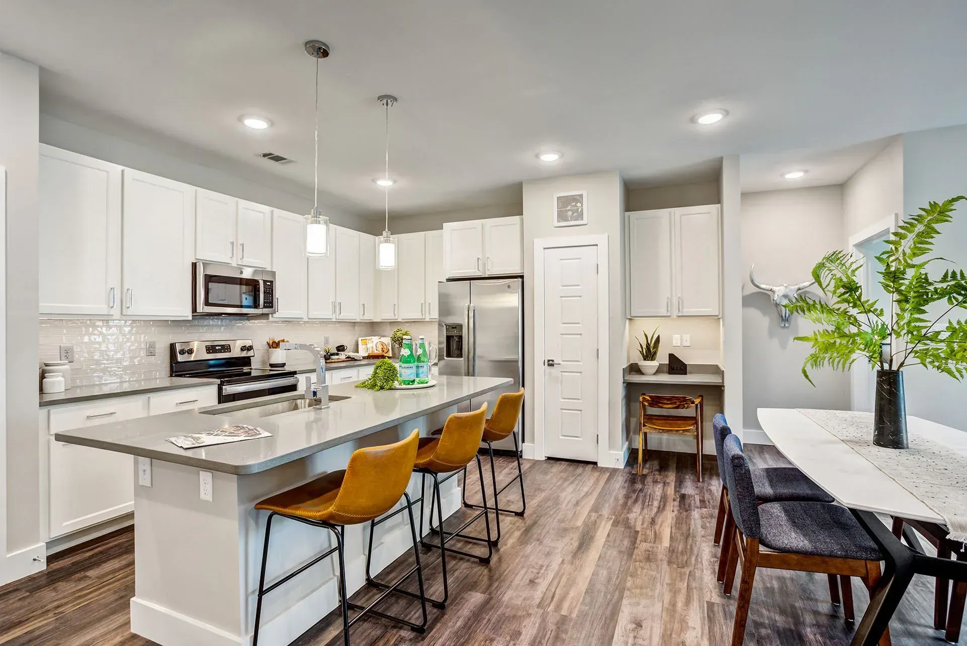 Modern kitchen with white cabinets, gray island with seating, stainless steel appliances, and wooden floor.