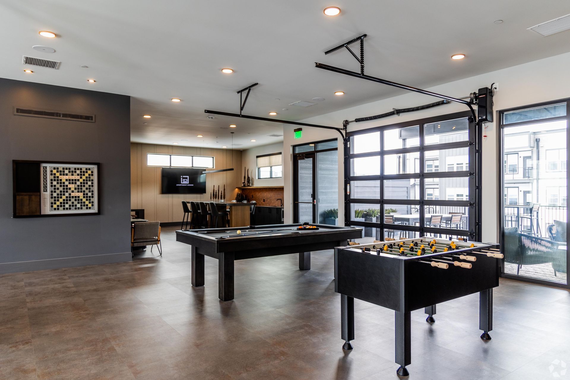Game room with foosball and pool tables, large windows, and dark accents.