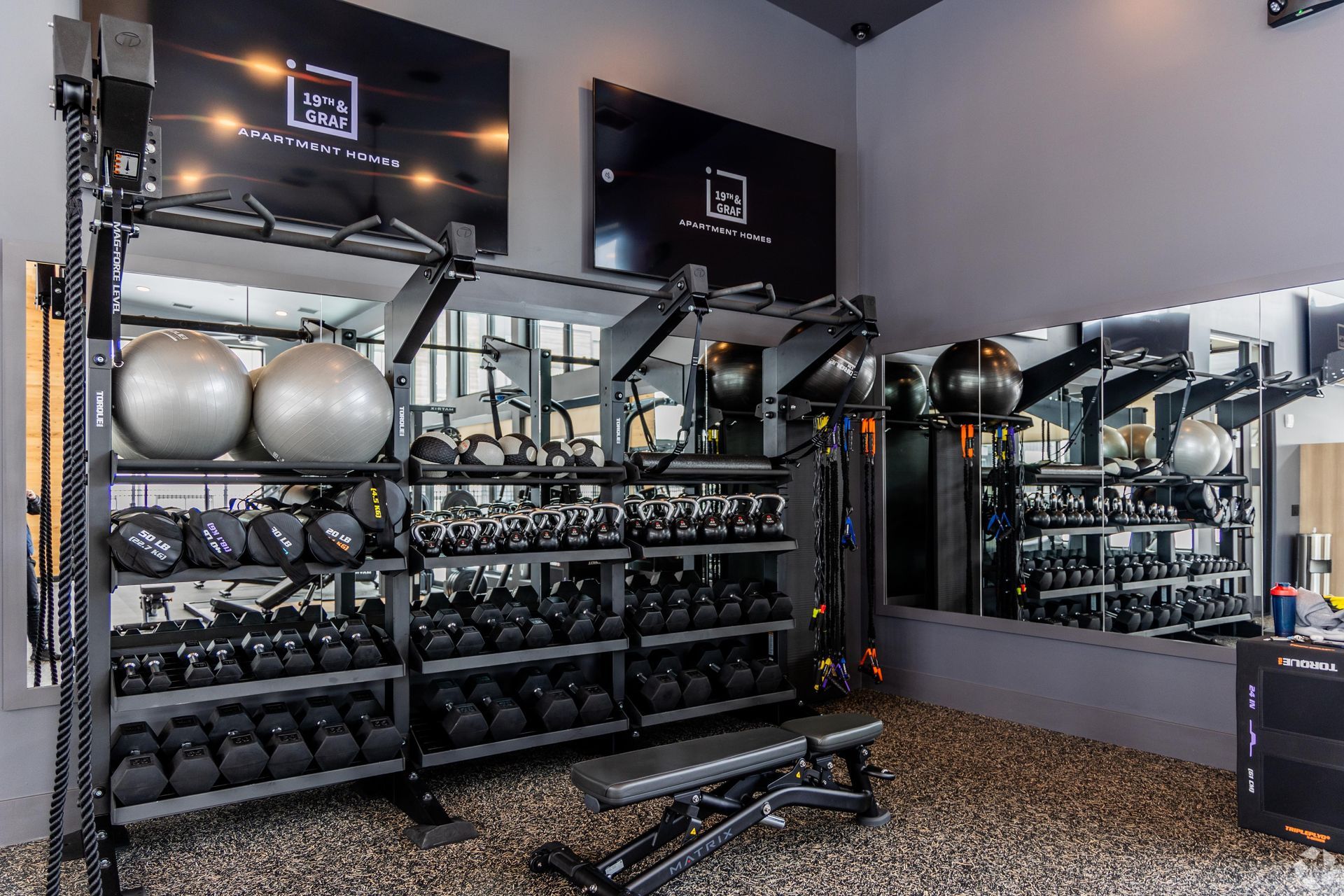 A well-equipped gym with black weights, exercise balls, and a bench.