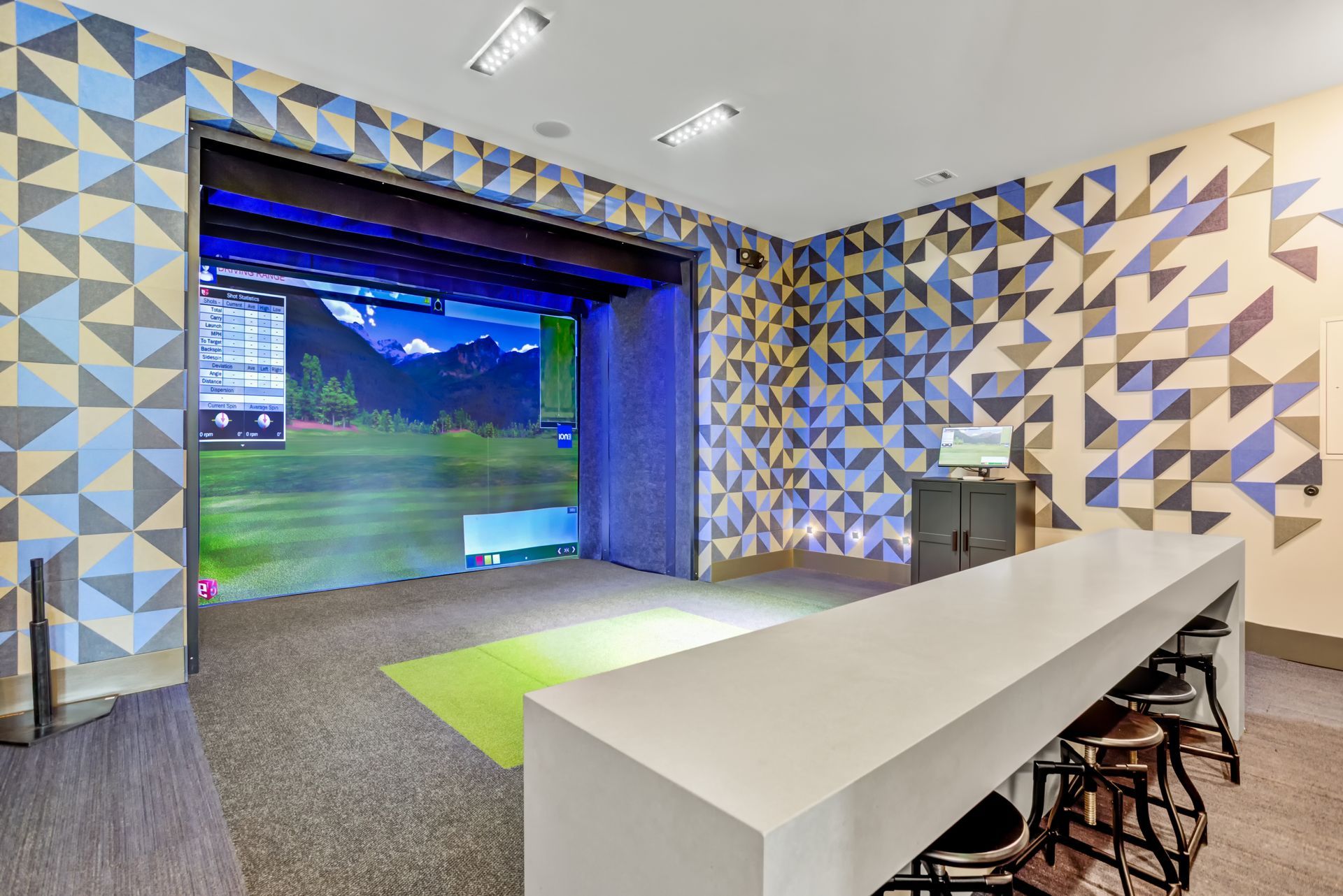 Indoor golf simulator room with a white counter and geometric patterned walls.
