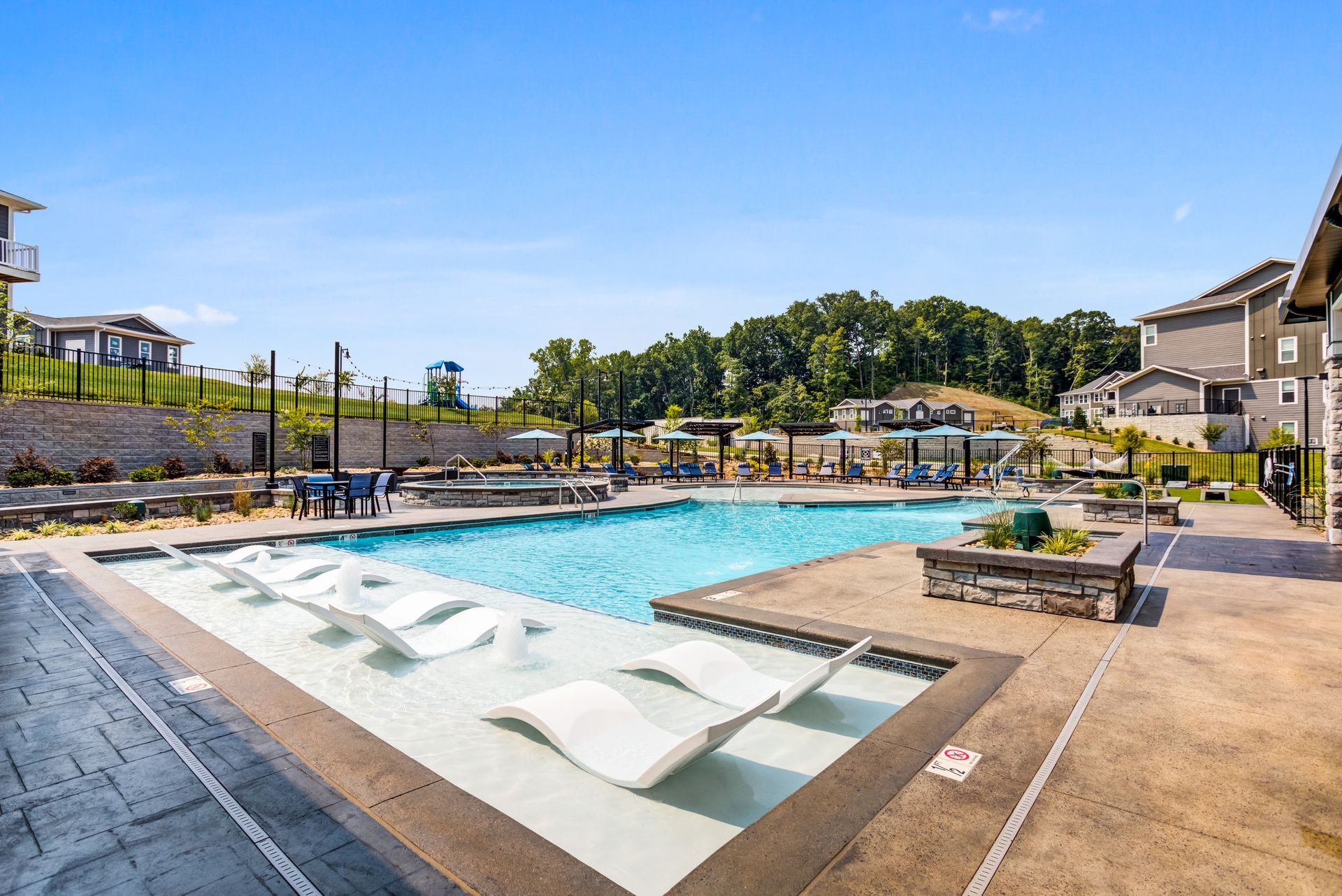 Pool with white lounge chairs, surrounded by concrete, and apartment buildings on a sunny day.