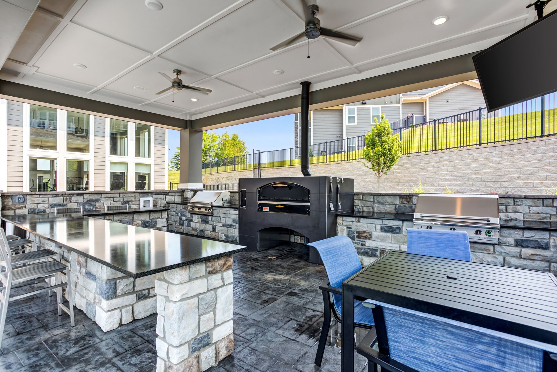 Outdoor kitchen with a pizza oven, grill, and seating under a covered patio.