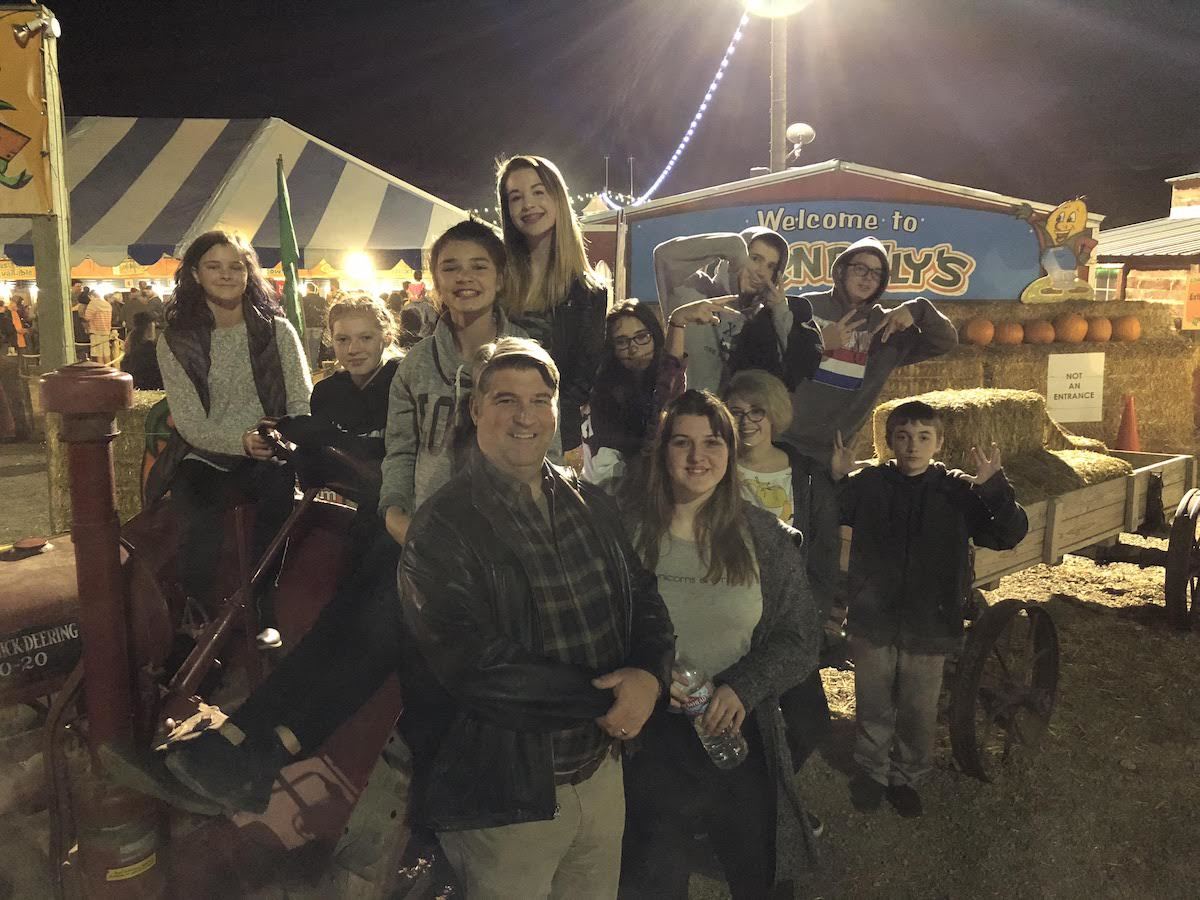 Group of people at a fair, posing on a tractor; night setting.