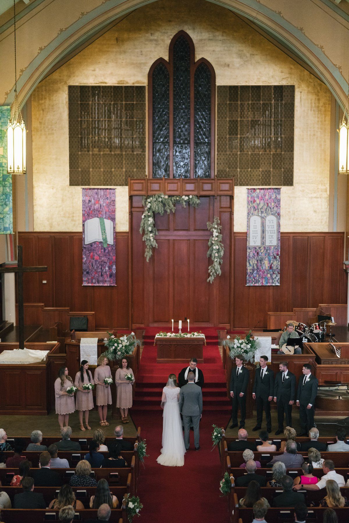 Wedding ceremony in a church with a bride and groom, bridal party, and seated guests.