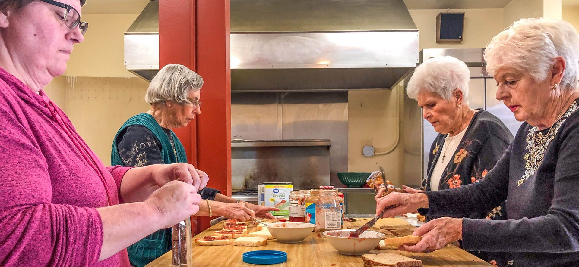 Four older women preparing food in a kitchen.