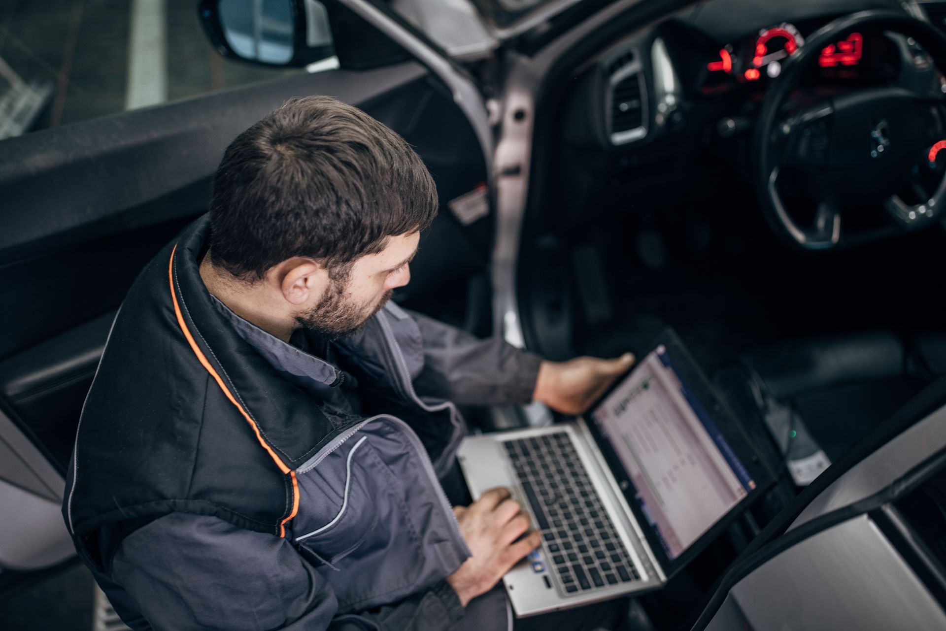 A man is sitting in a car using a laptop computer.