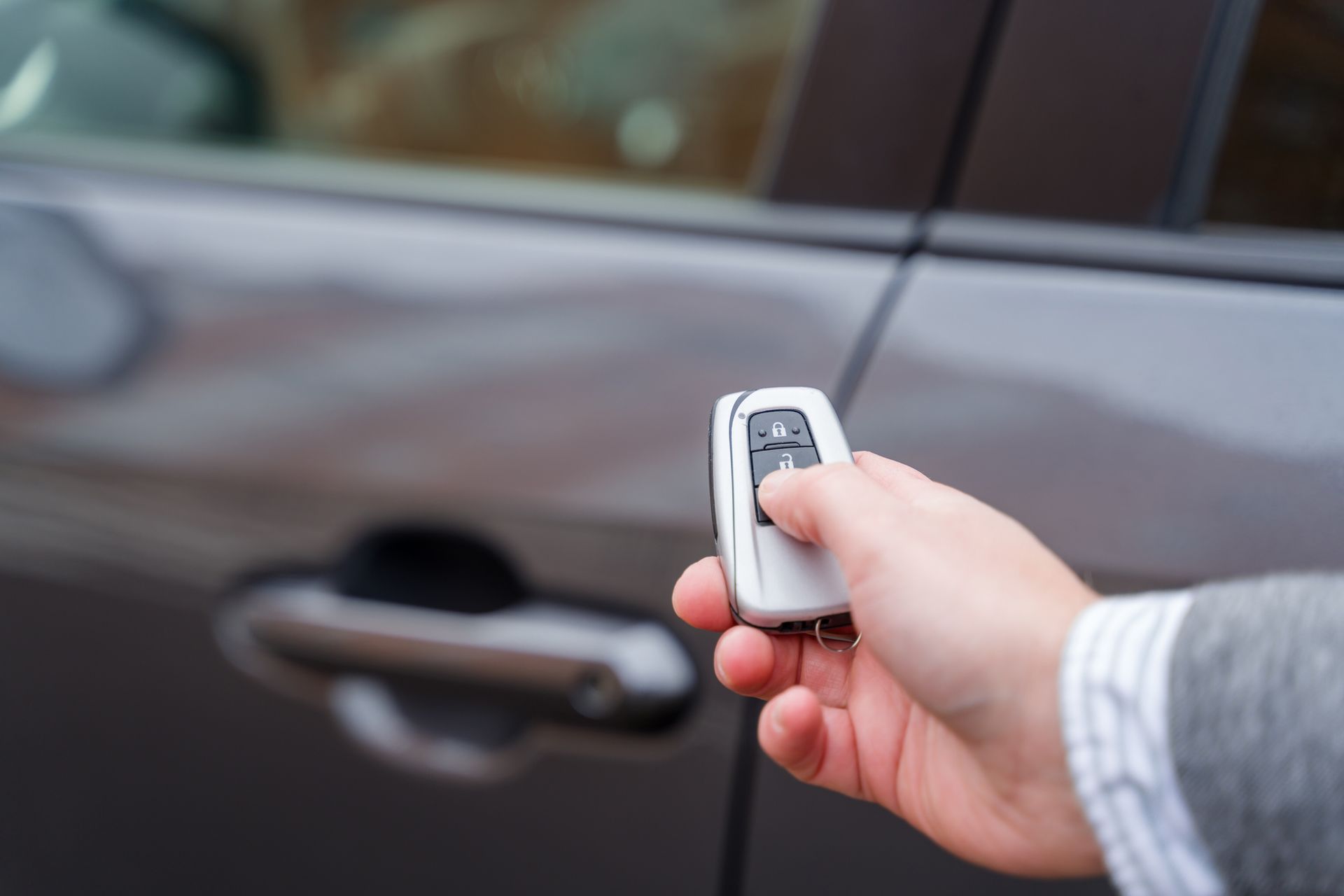 A person is holding a remote control in front of a car.