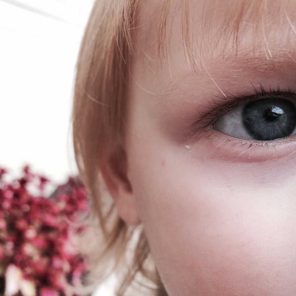 A close up of a child 's eye with a flower in the background.