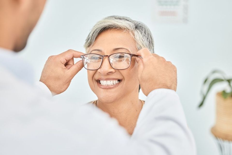 A man is helping an older woman put on glasses.