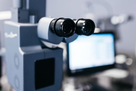 A close up of a microscope with a computer in the background.