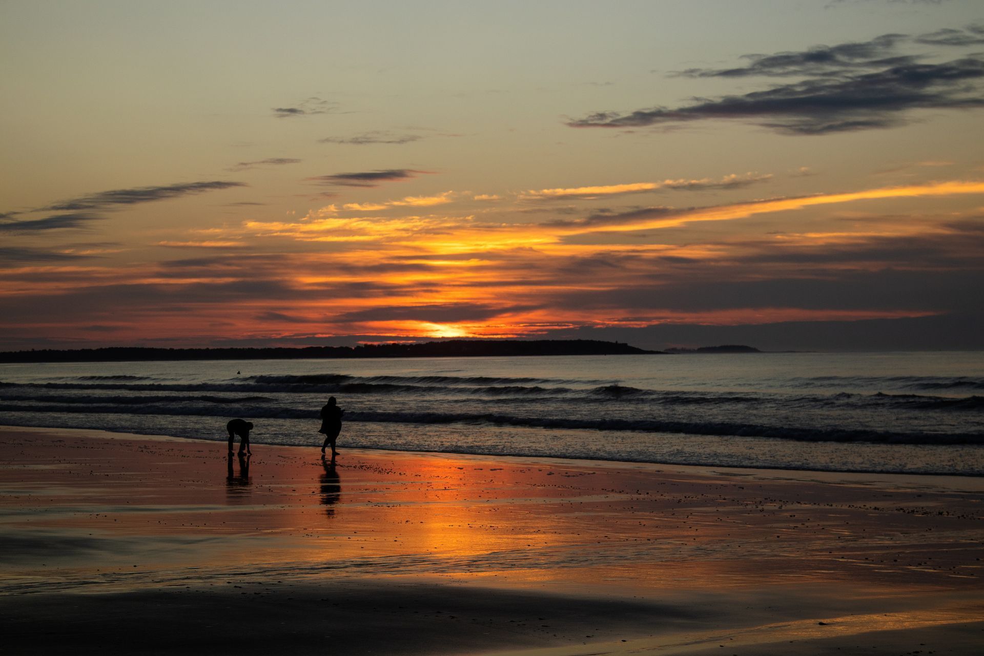 Sunset over a beach with two silhouetted figures on wet sand. 