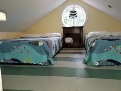 Loft bedroom with two beds, striped lamp, round window. 