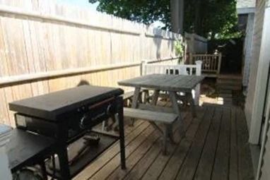 Outdoor deck with a grill and picnic table near a wooden fence.