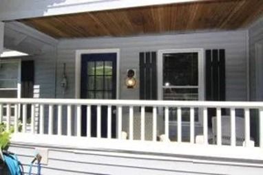 Front porch with white railing, blue door, and black shutters on a light gray house.