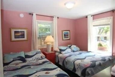Pink bedroom with two beds, two windows, and framed artwork.