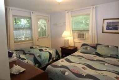 Bedroom with two beds, windows, and a nightstand with a lamp.