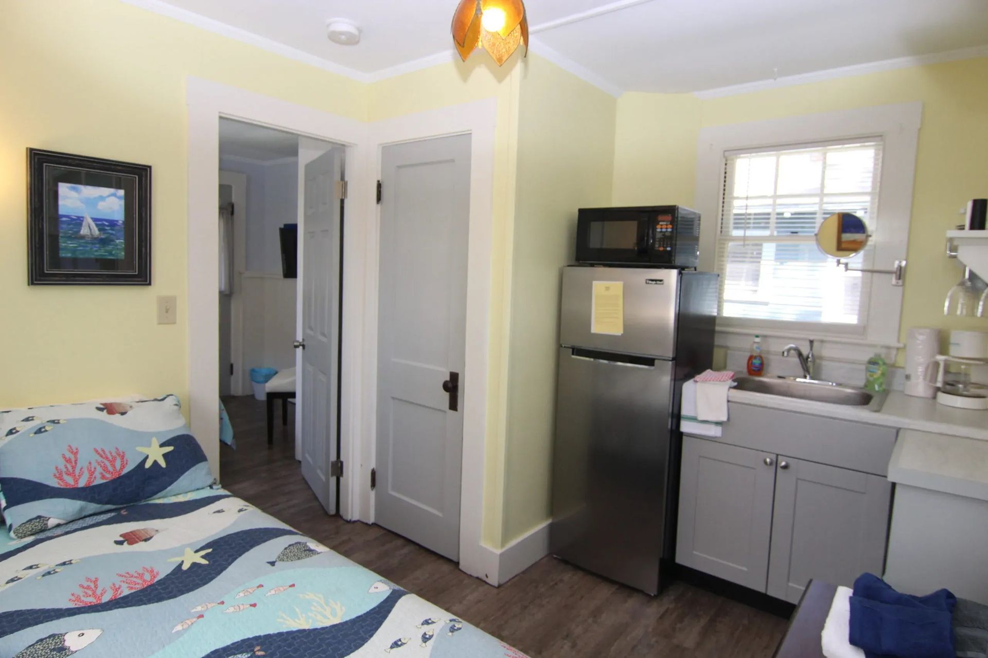Small studio apartment with bed, kitchenette, and doorway to another room.