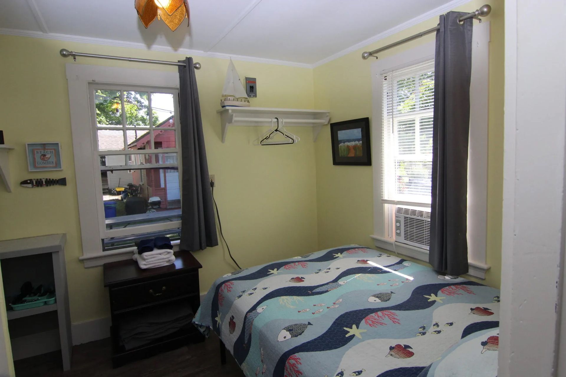 Small bedroom with windows, bed, and yellow walls. 
