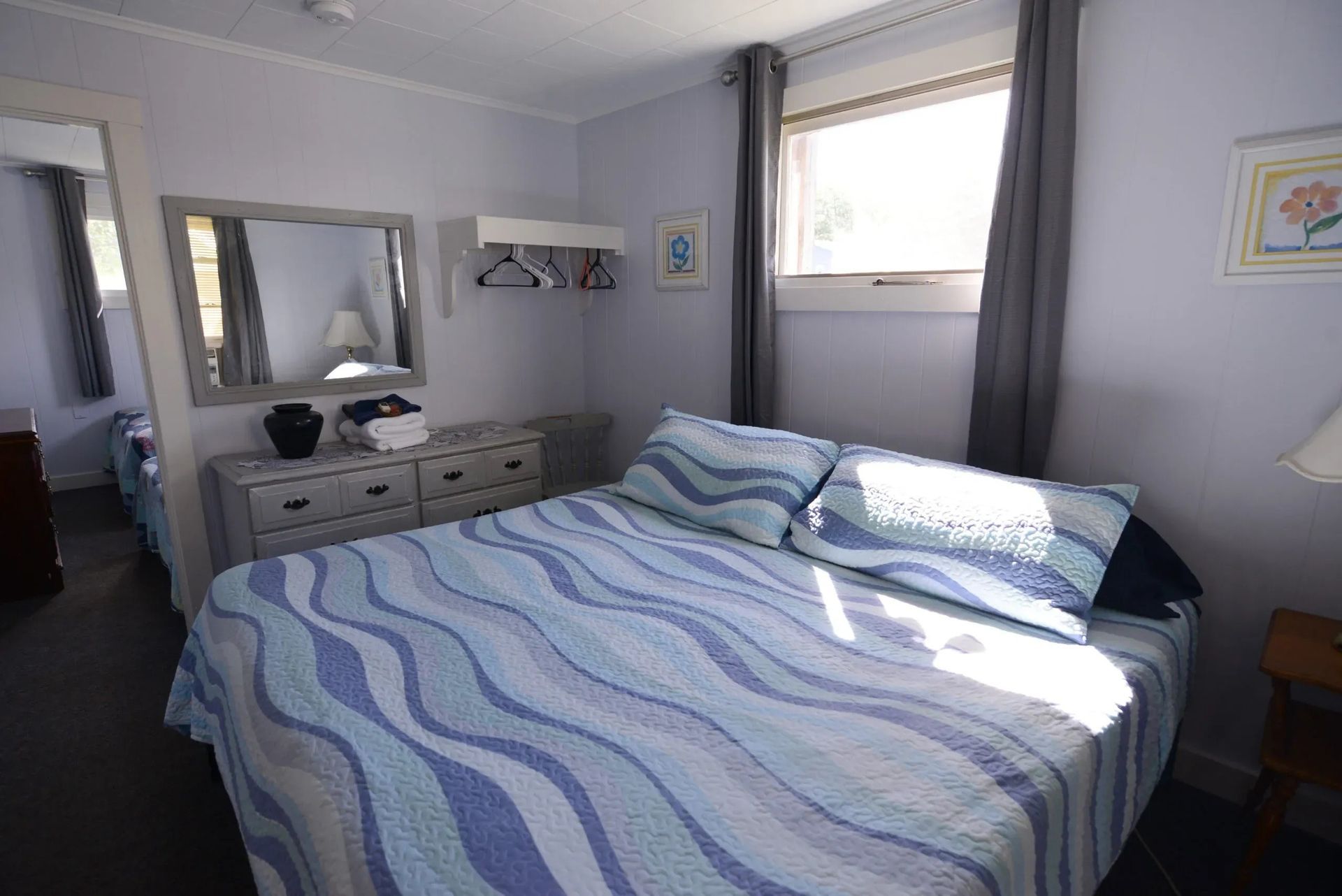 Bedroom with bed, dresser, mirror, window with curtains, and decorative items.