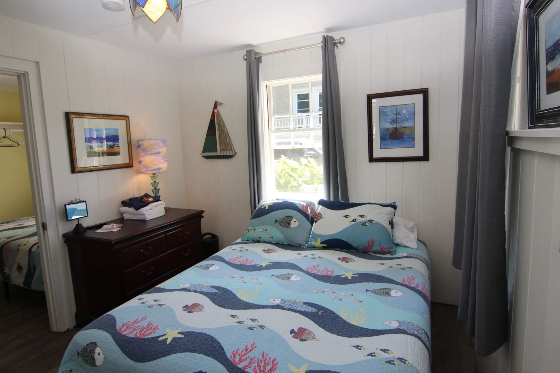 Bedroom with bed, dresser, window, paintings, and sailboat decor.