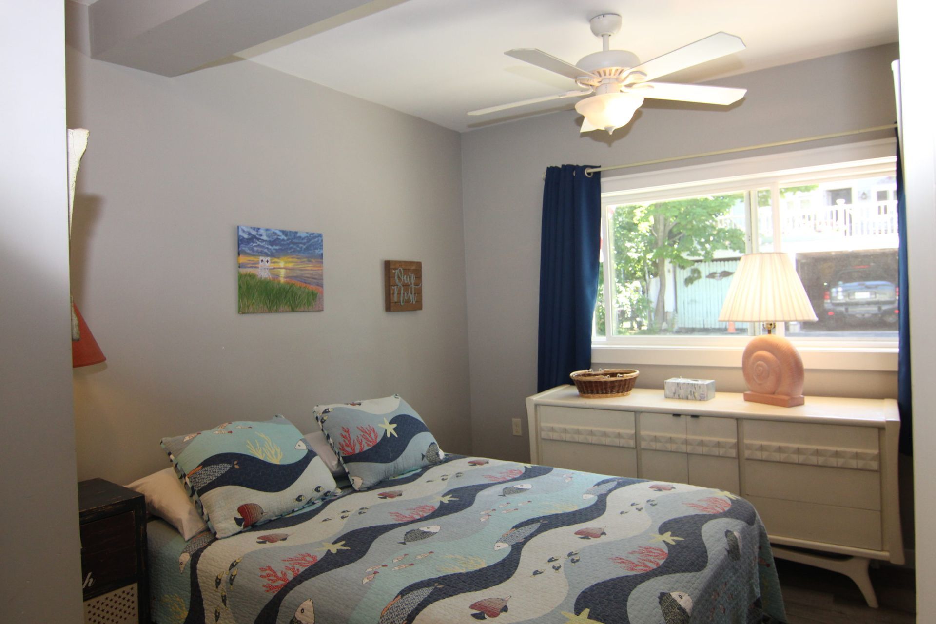 Bedroom with bed, dresser, window, artwork, and a ceiling fan.