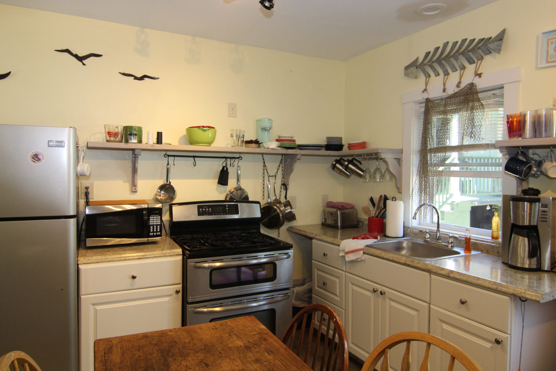 A small kitchen with stainless steel appliances, white cabinets, and a wooden table.