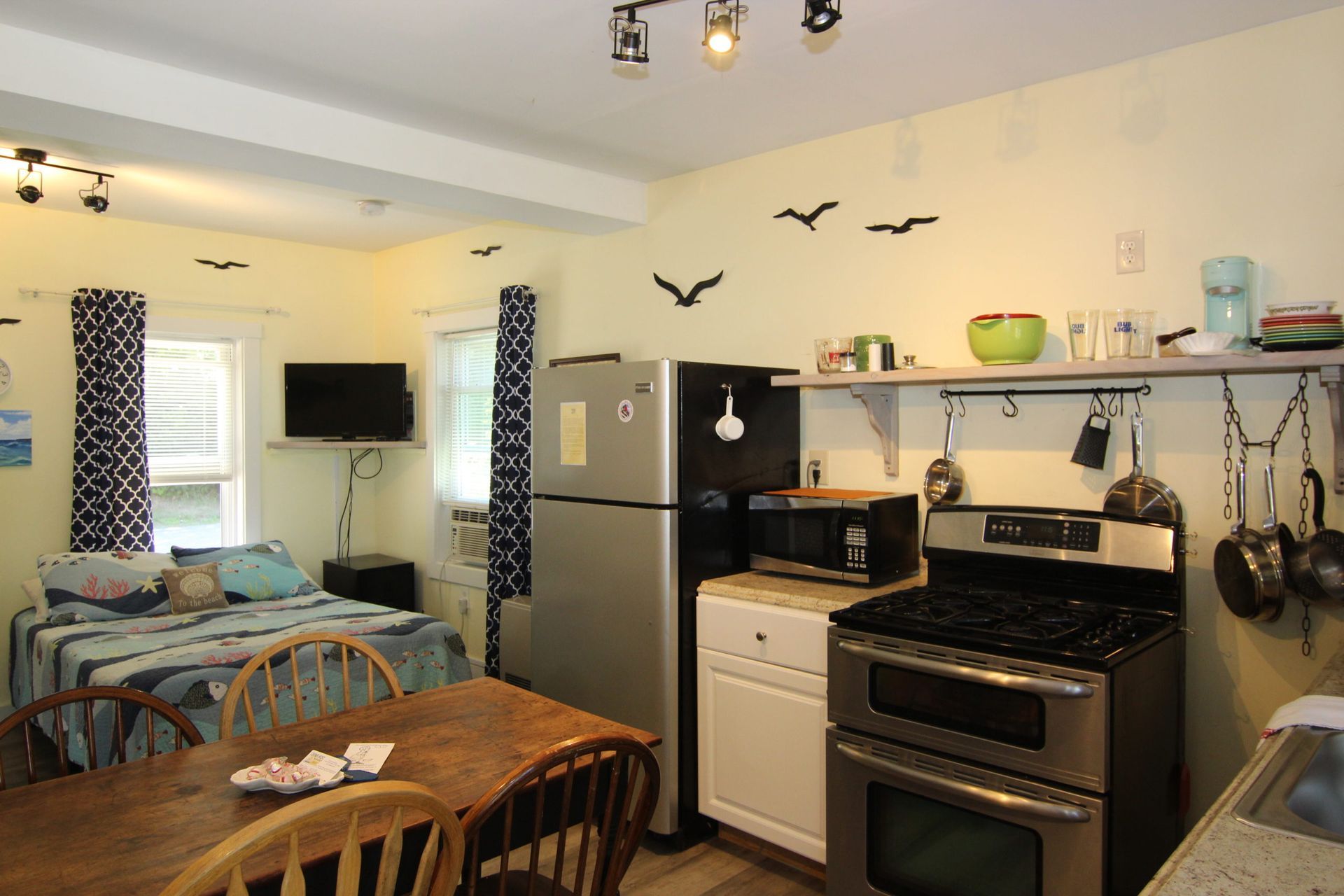 Cozy studio apartment with open kitchen, bed, dining table, and decorative birds on the yellow wall.