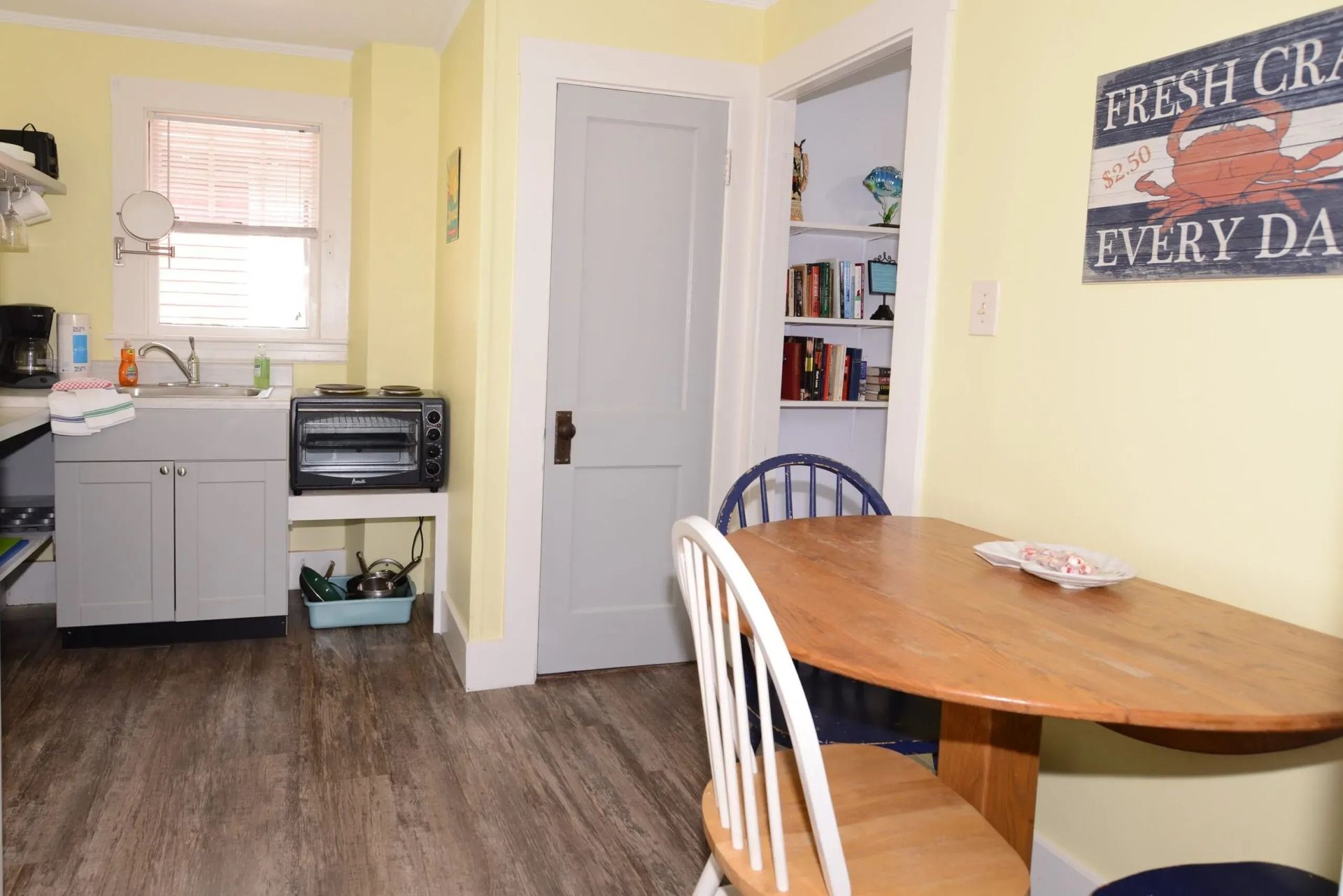 Cozy kitchen with a small table, cabinets, a sink, and a door leading to a bookshelf.